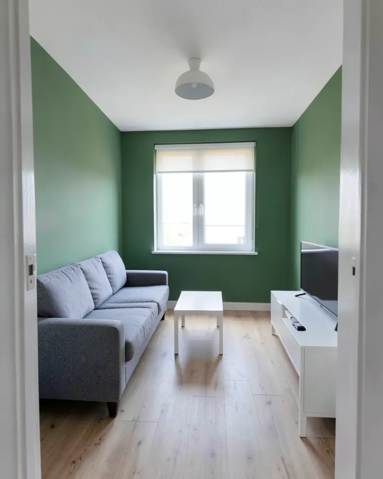 Dasselbe Wohnzimmer mit grünen Wänden und demselben grauen Sofa, weißen Couchtisch und TV-Board