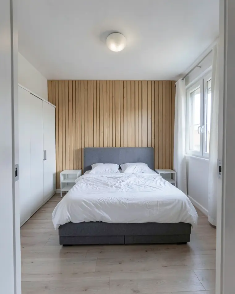 La stessa camera con doghe verticali in rovere chiaro sulla parete dietro il letto