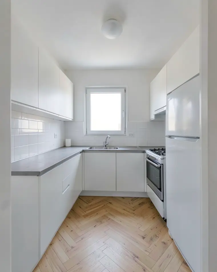 The same white kitchen with a light oak herringbone floor instead of the gray floor