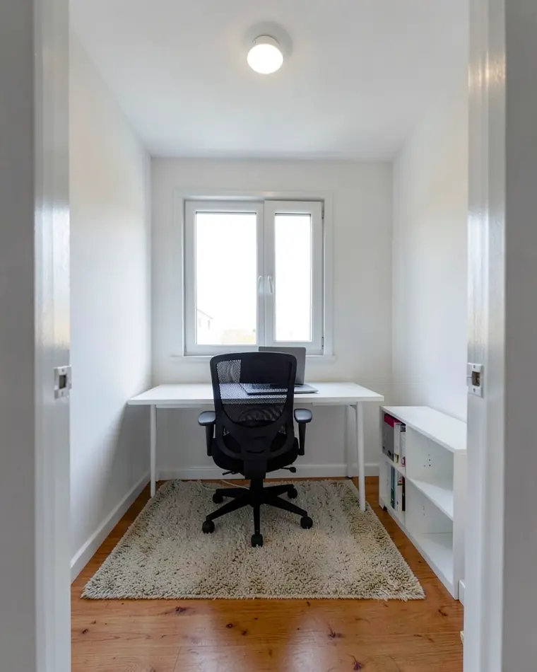 O mesmo home office com piso de tábuas de madeira em tom quente e um tapete felpudo bege embaixo da cadeira